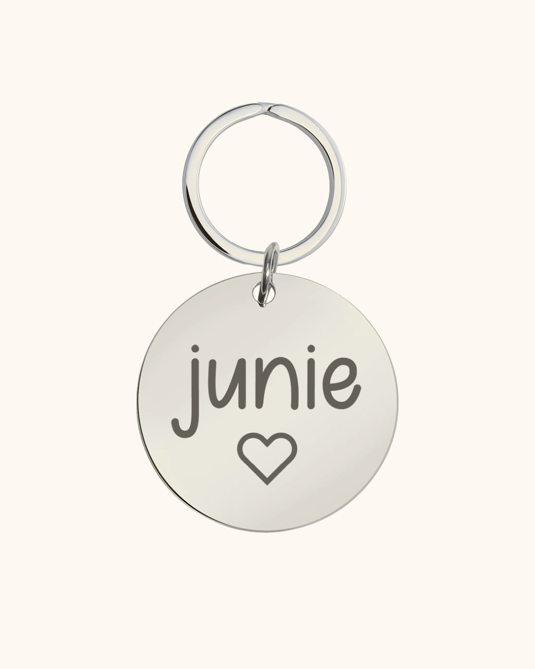 Round silver pet tag with 'junie' and a heart on a white background