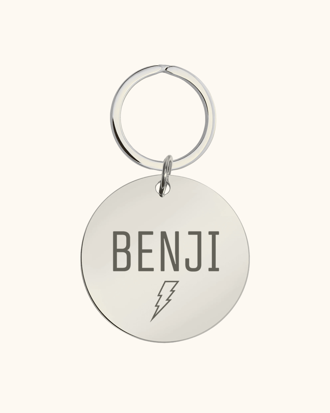 Silver pet tag with 'BENJI' and a lightning bolt on a white background